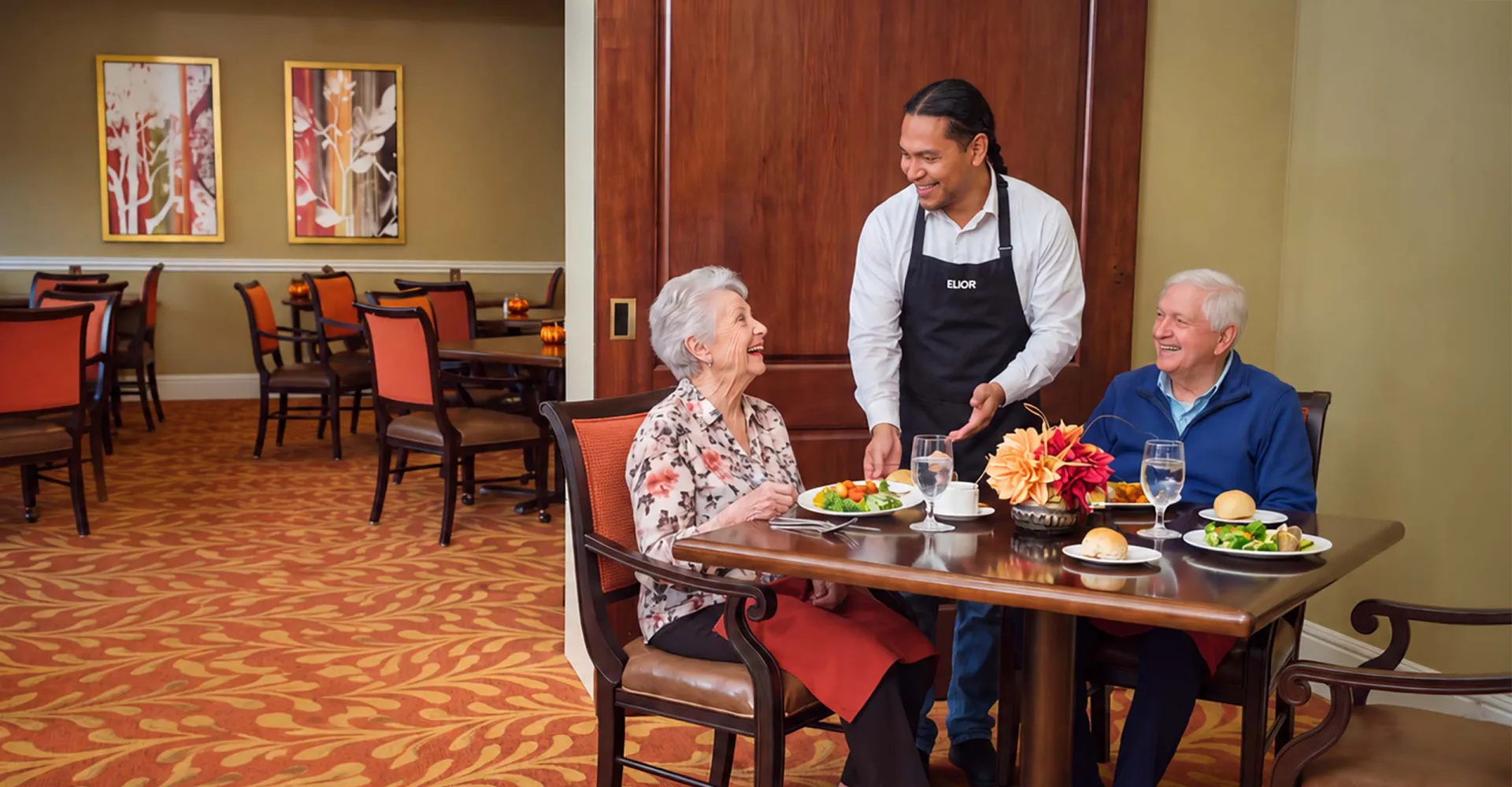 A dining room server presents a meal to a smiling older couple seated together at a table.