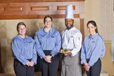A chef holding a plate of food while three servers stand beside him.